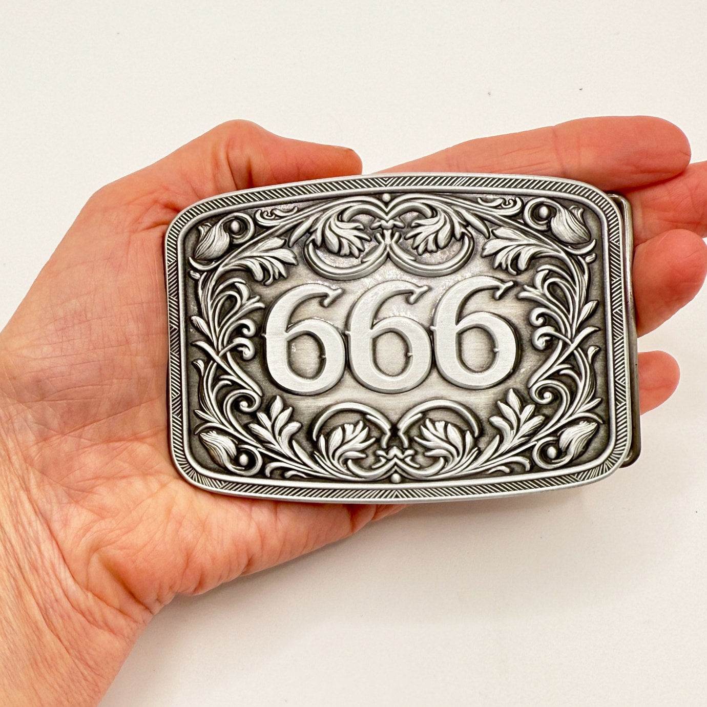 Goth Western 666 Belt Buckle with engraved centerpiece and floral scrollwork, held in hand.