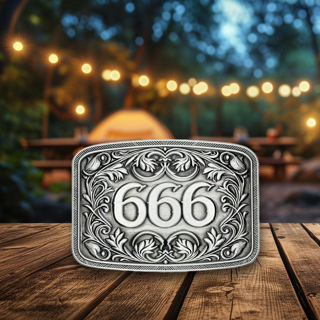 666 Belt Buckle with engraved floral scrollwork on wooden background.